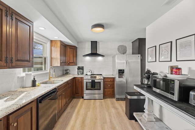 kitchen featuring tasteful backsplash, sink, stainless steel appliances, light wood-type flooring, and wall chimney exhaust hood