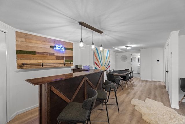 bar with hanging light fixtures, ornamental molding, and light hardwood / wood-style floors