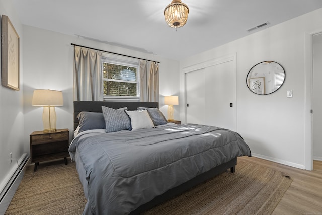 bedroom with baseboard heating, a closet, and hardwood / wood-style flooring