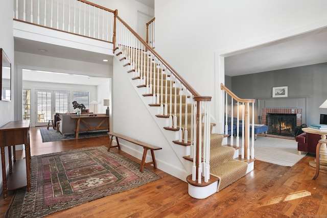 stairs with french doors, a fireplace, a towering ceiling, wood finished floors, and baseboards