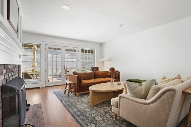 living room with french doors, recessed lighting, baseboard heating, a brick fireplace, and wood finished floors