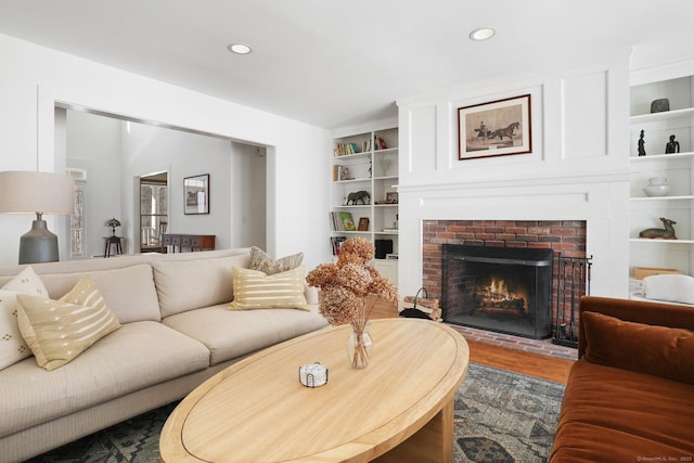 living room featuring built in features, recessed lighting, a brick fireplace, and wood finished floors