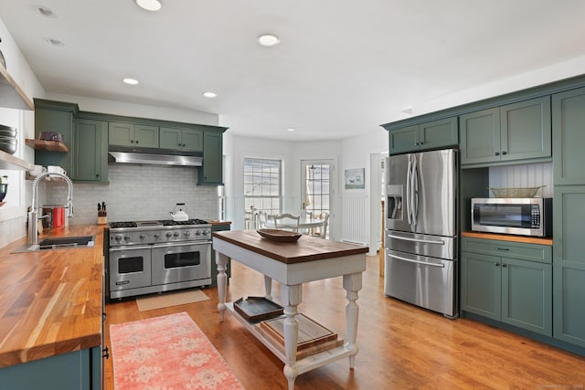 kitchen with under cabinet range hood, stainless steel appliances, butcher block countertops, a sink, and green cabinetry