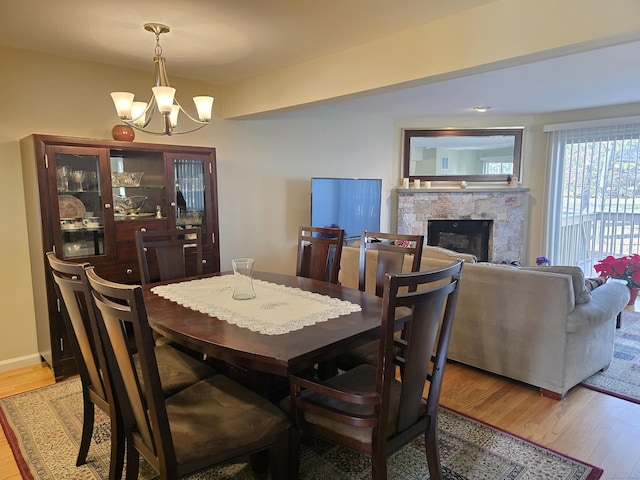 dining space with a stone fireplace, an inviting chandelier, and light wood-type flooring