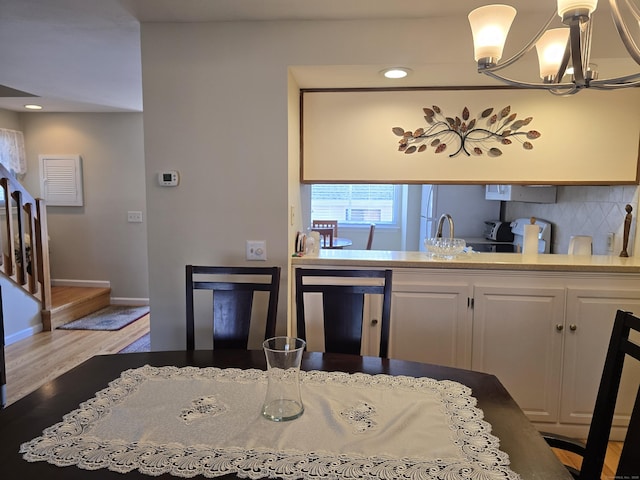 kitchen featuring pendant lighting, dishwashing machine, an inviting chandelier, decorative backsplash, and light wood-type flooring