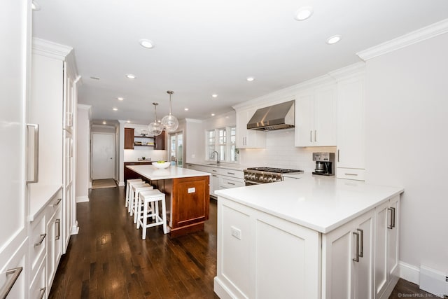 kitchen with white cabinets, high end range, a kitchen island, and wall chimney range hood