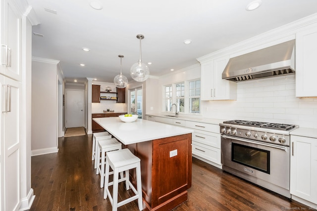 kitchen featuring wall chimney exhaust hood, dark hardwood / wood-style floors, stainless steel stove, a kitchen island, and white cabinets