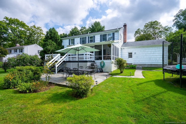 back of house featuring a lawn, a trampoline, a patio, a wooden deck, and a sunroom