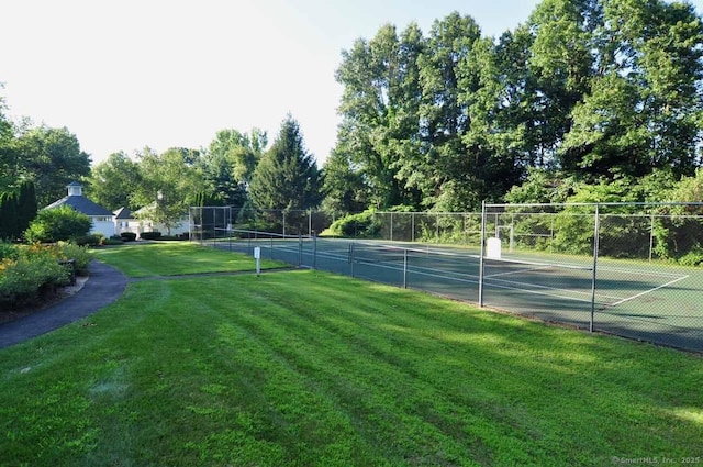view of tennis court featuring a lawn and fence