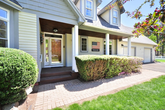 doorway to property with covered porch, driveway, a shingled roof, and a garage