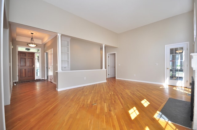 unfurnished living room with a healthy amount of sunlight, baseboards, ornate columns, and light wood-style flooring