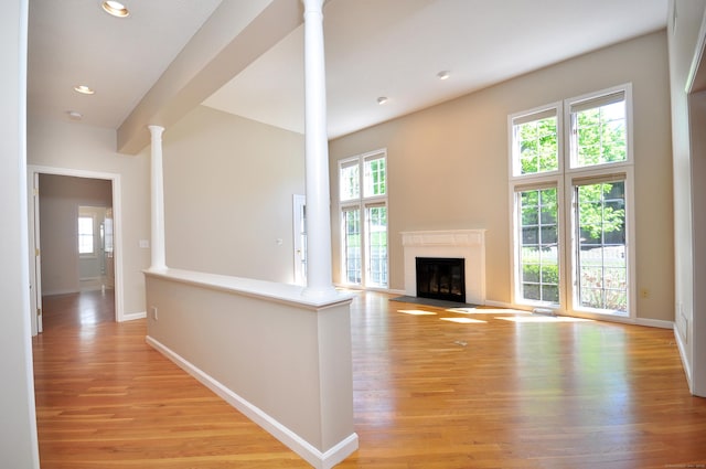 unfurnished living room featuring light wood-style floors, a fireplace with flush hearth, baseboards, and ornate columns