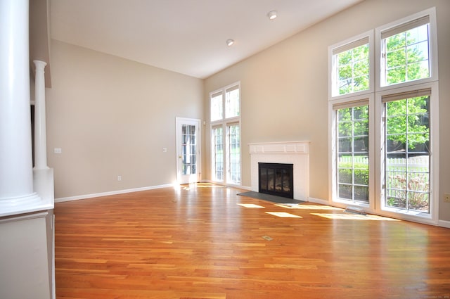 unfurnished living room with high vaulted ceiling, plenty of natural light, a fireplace, and light wood-type flooring