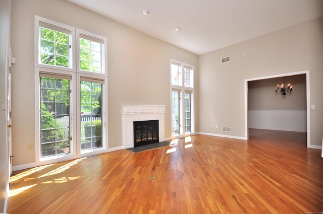 unfurnished living room featuring a notable chandelier, a brick fireplace, light wood-style flooring, and visible vents