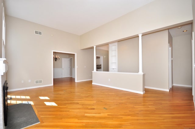unfurnished living room with an inviting chandelier, a fireplace, light wood-style flooring, baseboards, and visible vents