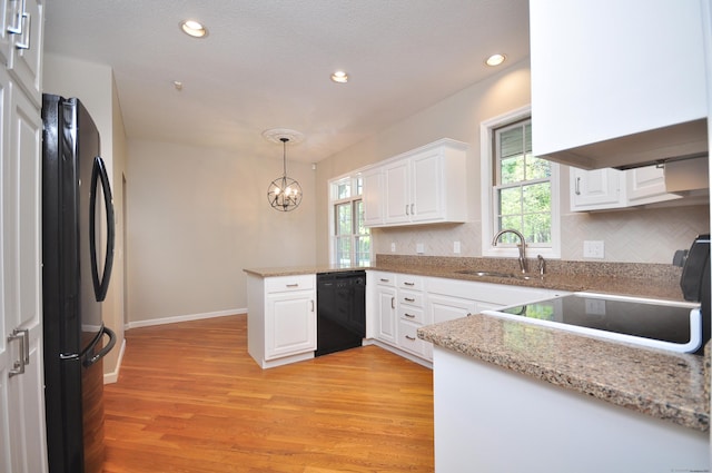 kitchen with a peninsula, black appliances, white cabinets, a sink, and a notable chandelier