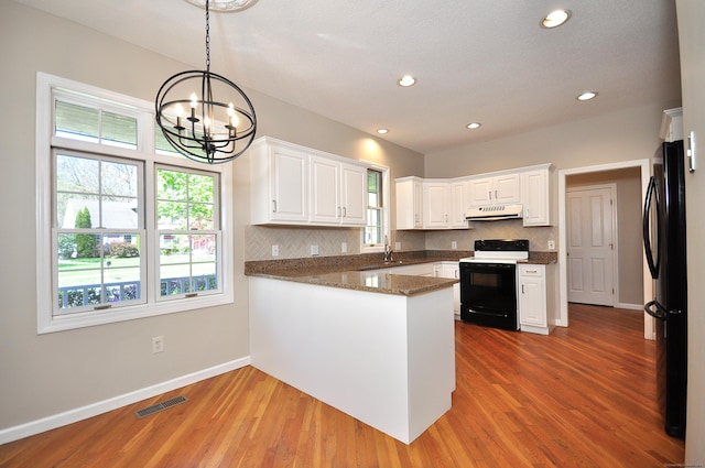 kitchen featuring freestanding refrigerator, a peninsula, baseboards, under cabinet range hood, and range with electric cooktop