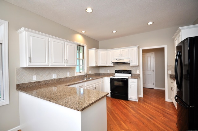 kitchen featuring freestanding refrigerator, a sink, under cabinet range hood, white cabinets, and electric stove