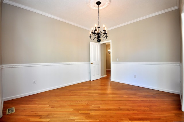 spare room with visible vents, ornamental molding, an inviting chandelier, and light wood finished floors
