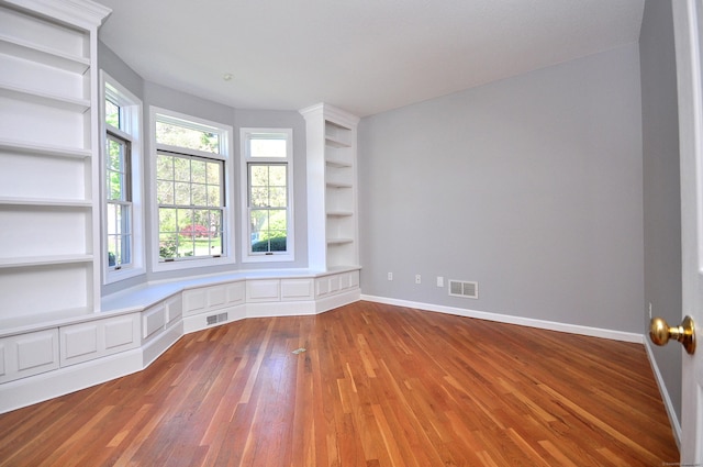 unfurnished room featuring visible vents, baseboards, wood finished floors, and built in features