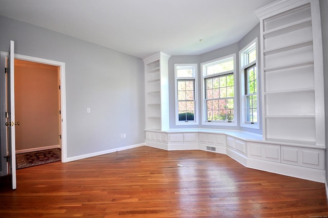 spare room with baseboards, built in features, wood finished floors, and visible vents