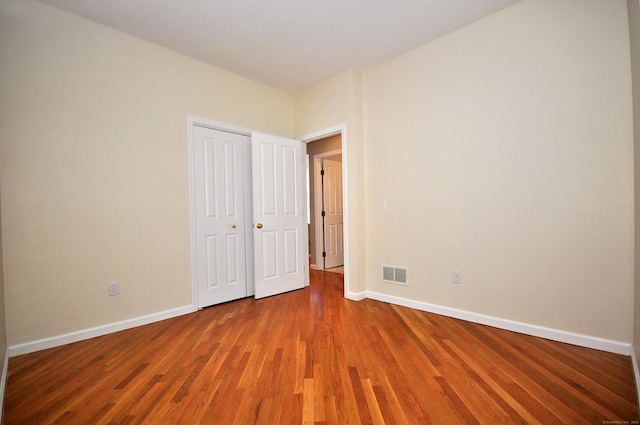 unfurnished bedroom with baseboards, wood finished floors, and visible vents