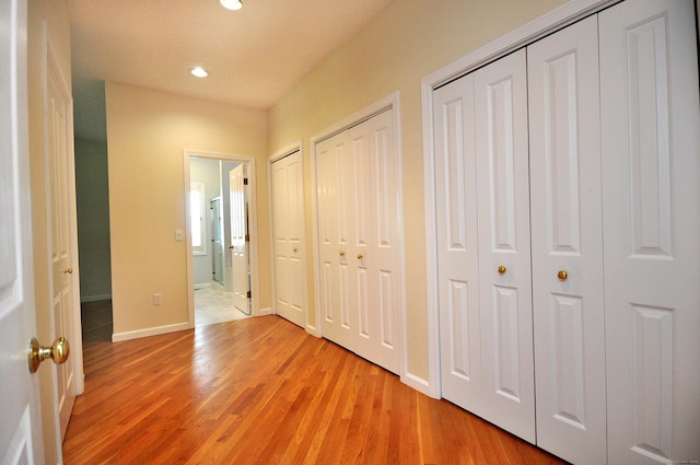 unfurnished bedroom with multiple closets, baseboards, light wood finished floors, and recessed lighting