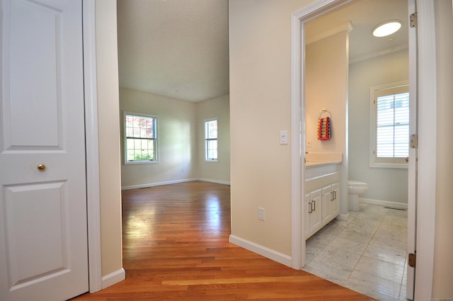 corridor with baseboards, ornamental molding, and light wood finished floors