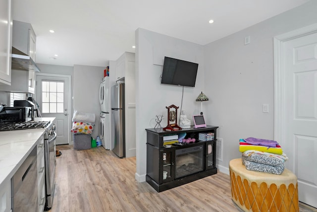 kitchen with appliances with stainless steel finishes, white cabinetry, stacked washer / drying machine, light stone countertops, and light hardwood / wood-style floors