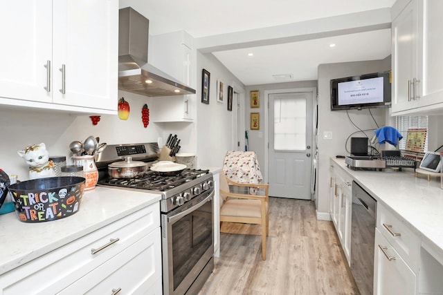 kitchen with white cabinetry, light hardwood / wood-style floors, stainless steel appliances, light stone countertops, and wall chimney exhaust hood