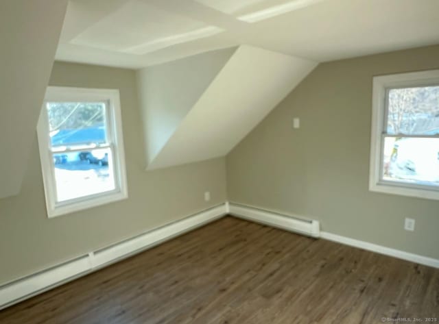 additional living space with vaulted ceiling, a healthy amount of sunlight, baseboard heating, and dark hardwood / wood-style flooring