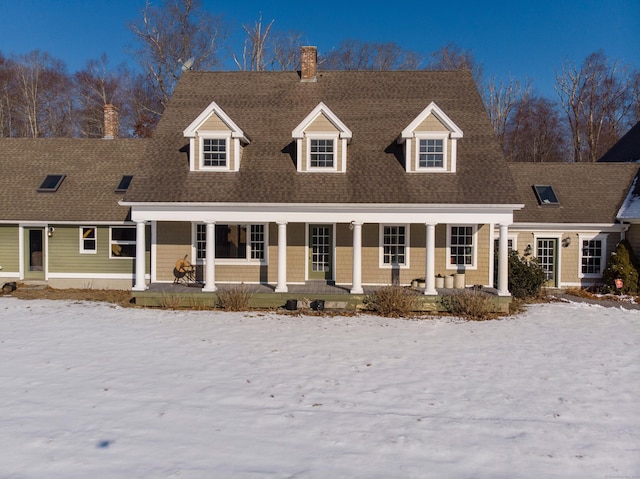 cape cod home with covered porch, a chimney, and roof with shingles