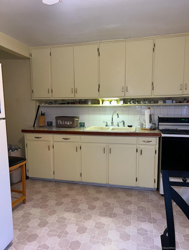 kitchen with tasteful backsplash, white fridge, sink, cream cabinetry, and range with electric stovetop