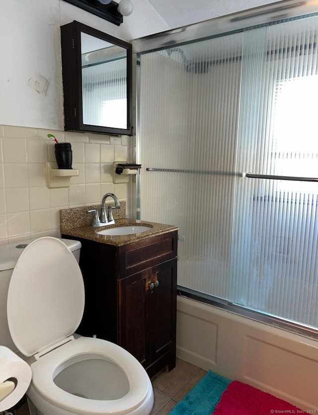 full bathroom with tile patterned flooring, enclosed tub / shower combo, tile walls, toilet, and vanity