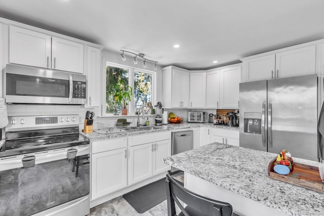 kitchen with sink, a breakfast bar, white cabinetry, stainless steel appliances, and light stone countertops