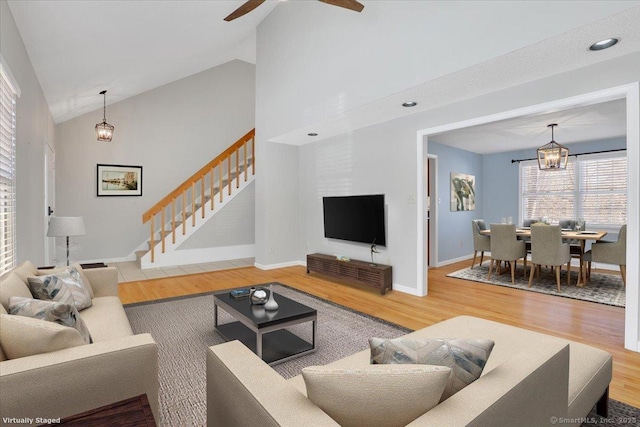 living room with high vaulted ceiling, wood-type flooring, and ceiling fan with notable chandelier