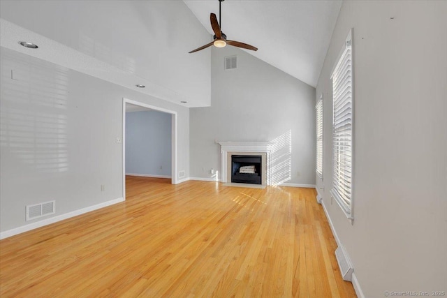 unfurnished living room with a wealth of natural light, vaulted ceiling, ceiling fan, and light wood-type flooring