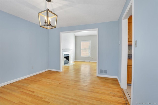 unfurnished living room with a textured ceiling, a chandelier, and light wood-type flooring