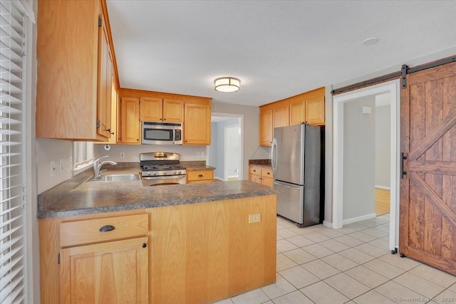 kitchen with light tile patterned flooring, sink, appliances with stainless steel finishes, kitchen peninsula, and a barn door