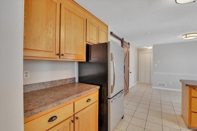 kitchen featuring a barn door, stainless steel fridge, light brown cabinetry, and light tile patterned floors