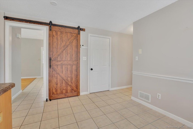 spare room with a barn door, a textured ceiling, and light tile patterned floors