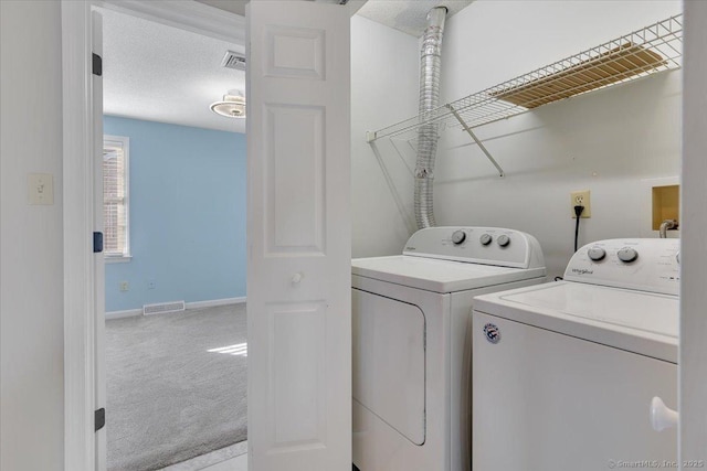 laundry area featuring light colored carpet, a textured ceiling, and washer and clothes dryer