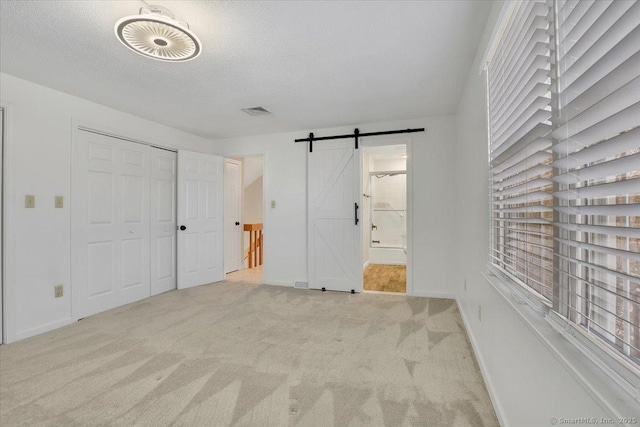 unfurnished bedroom featuring connected bathroom, a textured ceiling, a barn door, light carpet, and a closet