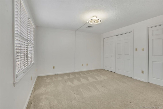 unfurnished bedroom featuring light carpet, multiple windows, and a textured ceiling