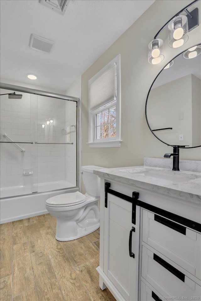 full bathroom featuring toilet, vanity, bath / shower combo with glass door, and hardwood / wood-style floors