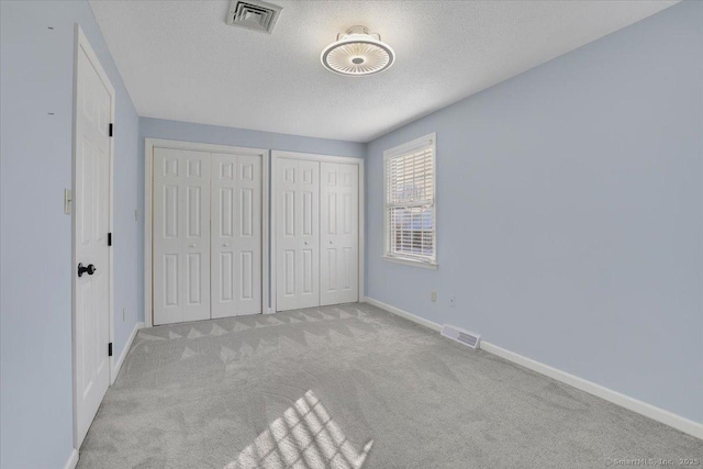 unfurnished bedroom with multiple closets, light carpet, and a textured ceiling