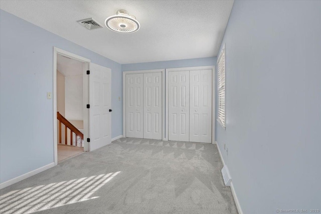 unfurnished bedroom featuring multiple closets, light colored carpet, and a textured ceiling