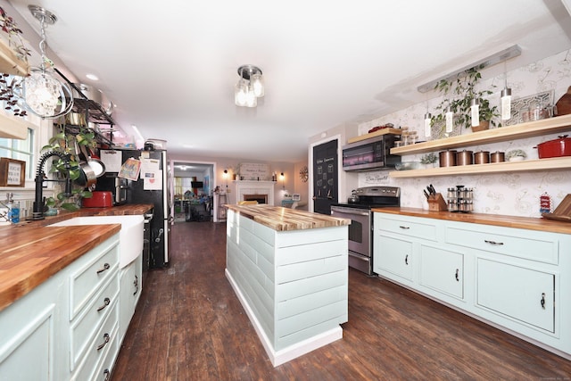 kitchen with a large fireplace, stainless steel appliances, butcher block counters, and hanging light fixtures