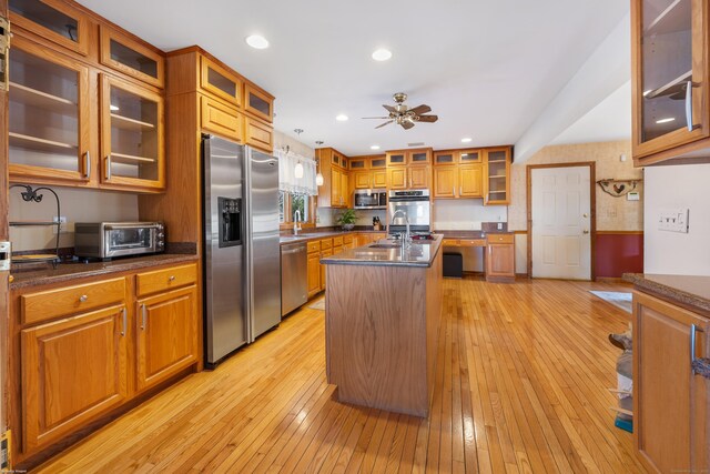 kitchen with sink, ceiling fan, a kitchen island with sink, stainless steel appliances, and light wood-type flooring