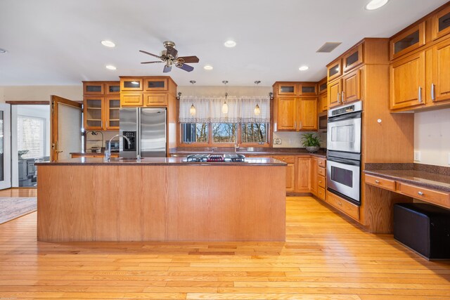 kitchen with light hardwood / wood-style flooring, ceiling fan, hanging light fixtures, stainless steel appliances, and a center island with sink